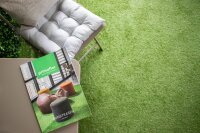 Eine lachende Frau mit lockigen, blonden Haaren sitzt barfuß im Schneidersitz auf einer begrünten Terrasse und arbeitet an einem Laptop. Um sie herum stehen mehrere Blumentöpfe mit verschiedenen Pflanzen. Im Hintergrund ein Metallgeländer mit weiteren Blumentöpfen. Im oberen Teil des Bildes steht der Text: Für ein tolles Ambiente, wobei das Wort tolles fett und rot unterstrichen ist.
