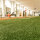 Innenaufnahme eines modernen Fitnessstudios mit künstlichem grünen Kunstrasen im Vordergrund, Trainingsgeräten und Hantelbänken im Hintergrund, die leicht unscharf sind. Die Räumlichkeiten sind hell beleuchtet und großzügig gestaltet.