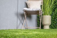 Moderne Terrasse mit Gartenmöbeln und roten Polstern auf einer Holzterrasse, davor ein kleiner Baum auf grünem Rasen; darüber der Text „Für ein tolles Ambiente“, wobei „tolles“ kursiv ist und rot unterstrichen.